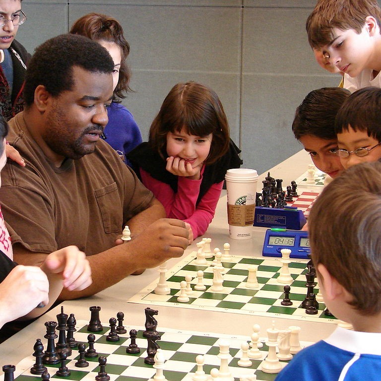 A group of children standby watching an adult playing a game of chess. A group of children standby watching an adult playing a game of chess.